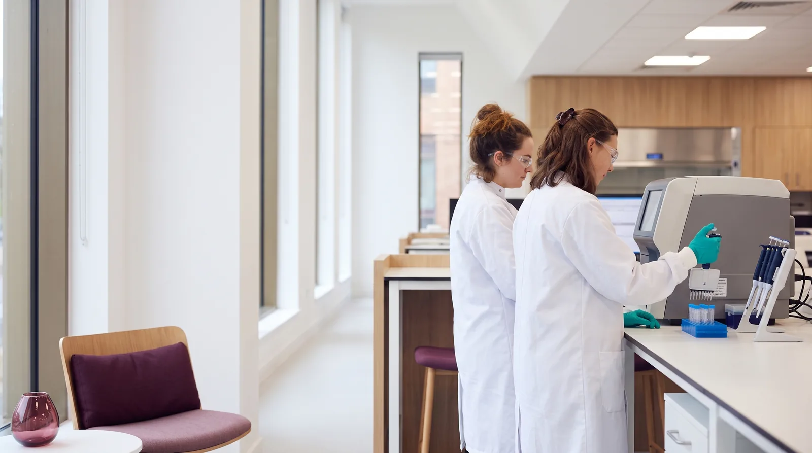 A wide, bright laboratory with professionals working at a clean bench and analyser